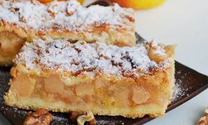 Kawałki domowej szarlotki posypane cukrem pudrem, z widocznymi jabłkami i orzechami. To szarlotka najlepsza jaką jadłam!