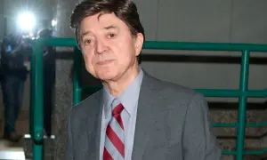 Jerzy Połomski w szarym garniturze i krawacie, otoczony przez błyski fleszy.