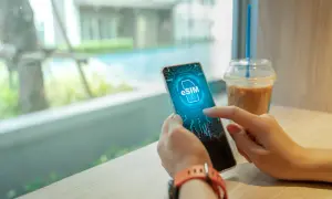 Dłoń trzyma smartfon z ikoną eSIM na ekranie, obok napoju.