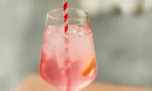 Erfrischender Sarti Spritz mit Eiswürfeln, einer Orangenscheibe und einem rot-weißen Strohhalm.