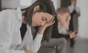 En ung kvinna med handen mot pannan, kanske i väntan på en **social fobi diagnos**. I bakgrunden syns andra personer.
