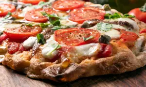 Knusprige Pizza mit Tomaten, Mozzarella und Basilikum auf einem Holzbrett.