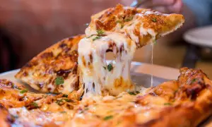 Ein Stück Pizza mit geschmolzenem Käse wird hochgehoben. Die vielen Pizza Kalorien sind es wert!