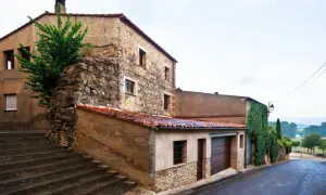 Escaleras de piedra suben hacia casas tradicionales de piedra y estuco, con tejados de teja roja. Una enredadera cubre parte de una pared.