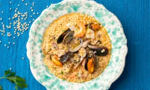 Piatto di fregola con pesce, cozze, vongole e gamberi, guarnito con prezzemolo tritato.
