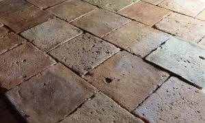 Carrelage en terre cuite, aspect brut et texturé. Chaque carreau présente des variations de couleur et de petites imperfections, témoignant d'un traitement artisanal.