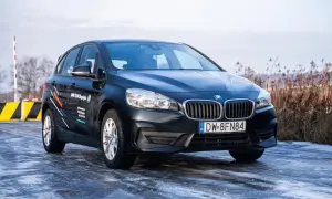 Ciemny BMW 218i na oblodzonej drodze, z logo BMW TEAM Długołęka na drzwiach.