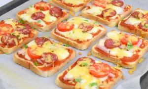 Pyszne pizza z chleba tostowego z serem, pomidorami i kiełbasą, gotowa do pieczenia.