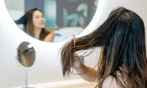 Mujer se peina el pelo graso frente a un espejo iluminado.