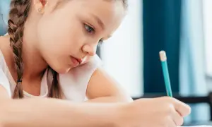 Bambina concentrata scrive con matita. Potrebbe essere una di quei bambini plusdotati 2 anni che già imparano a scrivere.