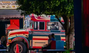Bunter "chicken bus" in Guatemala, bereit für die nächste Fahrt. Menschen warten auf dem Bürgersteig.