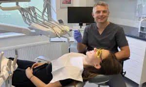 Dentysta w rękawiczce trzyma wiertło, pacjentka w okularach ochronnych leży na fotelu.