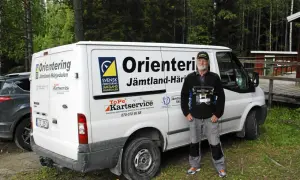 Torgny Pettersson står bredvid en vit skåpbil med texten "Orientering Jämtland-Härjedalen". Han håller i en utrustning för orientering.