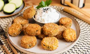 Knusprig panierte Zucchini-Taler auf einem Teller, serviert mit einem Dip und garniert mit Petersilie. Ein leckerer Snack!