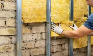 Pracownik w białych rękawicach montuje wełnę mineralną na stelażu, pokazując jak ocieplić fundamenty starego domu.