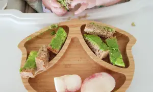Babyhände greifen nach Avocado-Brotstücken auf einem Holzbrett. Ein 10 Monate altes Baby erkundet sein Essen.
