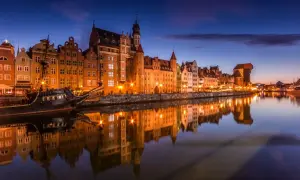 Gdańsk nocą, z zabytkowymi kamienicami i żaglowcem odbijającymi się w spokojnej wodzie Motławy.
