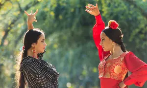 Dos bailarinas de un grupo flamenco famoso, con trajes vibrantes, ejecutan pasos elegantes bajo la luz del sol.