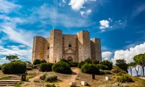 Castel del Monte, un'imponente fortezza ottagonale, si erge su una collina sotto un cielo azzurro e nuvoloso. Un luogo perfetto per chi ama visitare Castel del Monte.