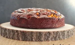 Torta al cioccolato con pezzi di mango, spolverata di zucchero a velo, su un tagliere di legno grezzo.