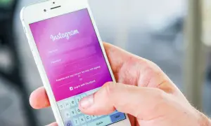 Dłoń trzyma smartfon z ekranem logowania Instagram. Widoczna opcja "Zapomniane dane logowania?" podpowiada, jak odzyskać hasło na Instagramie.