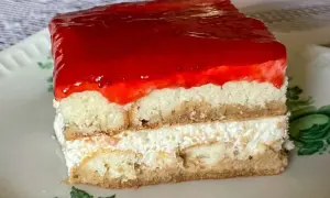 Kawałek ciasta bez pieczenia z warstwami biszkoptu, kremu i galaretki truskawkowej na talerzyku.