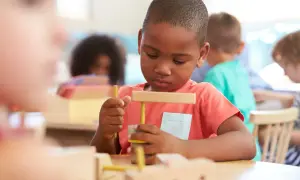 Ein Junge in einer Montessori-Schule baut konzentriert mit Holzbausteinen. So lernt man hier spielerisch.