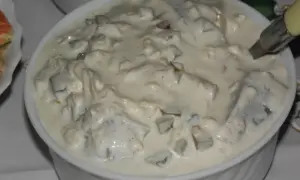 Pyszne śledzie w śmietanie, z kawałkami ogórka i cebuli, gotowe do podania.