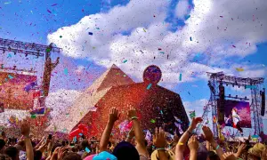 Confetti rains down on a cheering crowd at the Glastonbury Pyramid Stage, a vibrant celebration under a blue, cloud-filled sky.