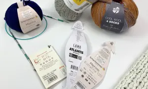 Wollknäuel zeigen den Unterschied zwischen Schurwolle und Wolle. Ein blauer Merino-Strang und ein Tweed-Garn liegen neben Stricknadeln.