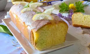 Un delizioso plumcake al limone glassato, decorato con fette di limone e menta, pronto per essere gustato.