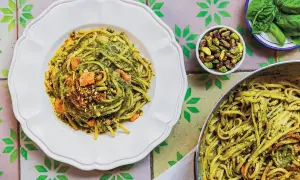 Makaron linguine z zielonym pesto, pistacjami i kawałkami łososia na białym talerzu.