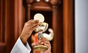Dłonie kapłana w białej albie trzymają złoty kielich z hostią, celebrując sakrament eucharystii.