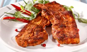 Grillowany boczek w aromatycznej marynacie, podany z papryczkami chili i zielonymi ziołami. Idealny na letnie przyjęcie.