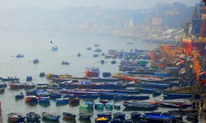 Łodzie na rzece Ganges, w tle mgliste miasto z budynkami i świątyniami.