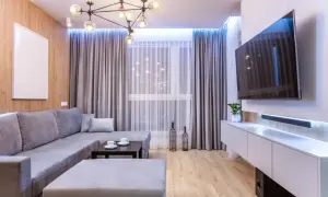 Nowoczesny salon w małym mieszkaniu 40 m: szara sofa, stolik kawowy, TV na ścianie i drewniana ściana.