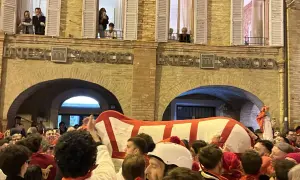 Folla festante al carnevale di Offida, con un grande carro bianco e rosso che avanza tra la gente.