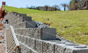 Budowa muru oporowego z betonowych bloków, z drabiną i sznurkiem do poziomowania. Kara za mur oporowy? Nie, to inwestycja w stabilność skarpy.