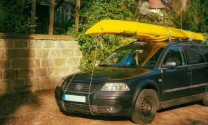 Żółty kajak na dachu czarnego kombi. Pokazuje, co można przewozić na dachu samochodu, np. sprzęt wodny.
