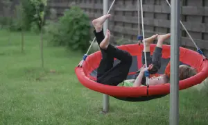 Dzieci bawiące się na czerwonej huśtawce bocianie gniazdo w ogrodzie.