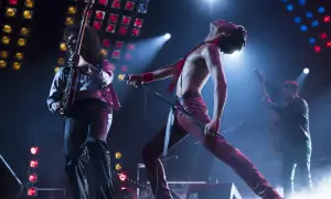 Freddie Mercury w czerwonym stroju, śpiewający na scenie, podczas gdy gitarzysta gra. To jest ich queen rhapsody.