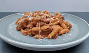 Gnocchi Sardi (Malloreddus) mit Tomatensoße und geriebenem Parmesan auf einem Teller.