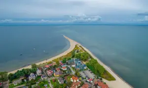 Malownicza miejscowość nad morzem z zabudowaniami i piaszczystą plażą, otoczona spokojnymi wodami.