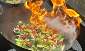 Ogień buchający z woka podczas przygotowywania pysznego stir fry z warzywami.