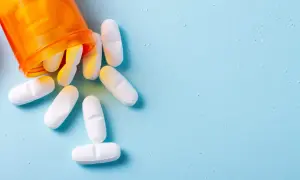 Białe tabletki, w tym euthyrox 25, wysypują się z pomarańczowego pojemnika na jasnoniebieskim tle.