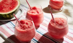 Fryst sallad med vattenmelon i glas med randiga sugrör. En halv vattenmelon ligger bredvid.