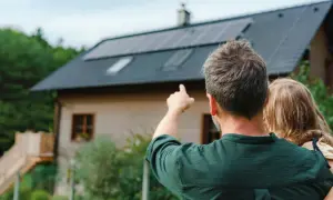 Hombre señala las placas solares virtuales en el tejado de una casa, mientras abraza a una niña.