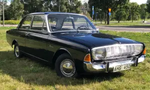 Svart Ford Taunus 1964, en klassisk bil med kromdetaljer, parkerad på en gräsmatta.