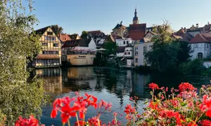 Blick auf Bamberg mit Fachwerkhäusern am Fluss. Rote Geranien im Vordergrund. Entdecken Sie Bamberg Geheimtipps!