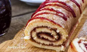Un delizioso rotolo alla marmellata, spolverato di zucchero a velo e decorato con un filo di confettura rossa, pronto per essere gustato.